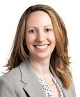 Headshot: Woman in polka dot top and grey jacket smiling at the camera